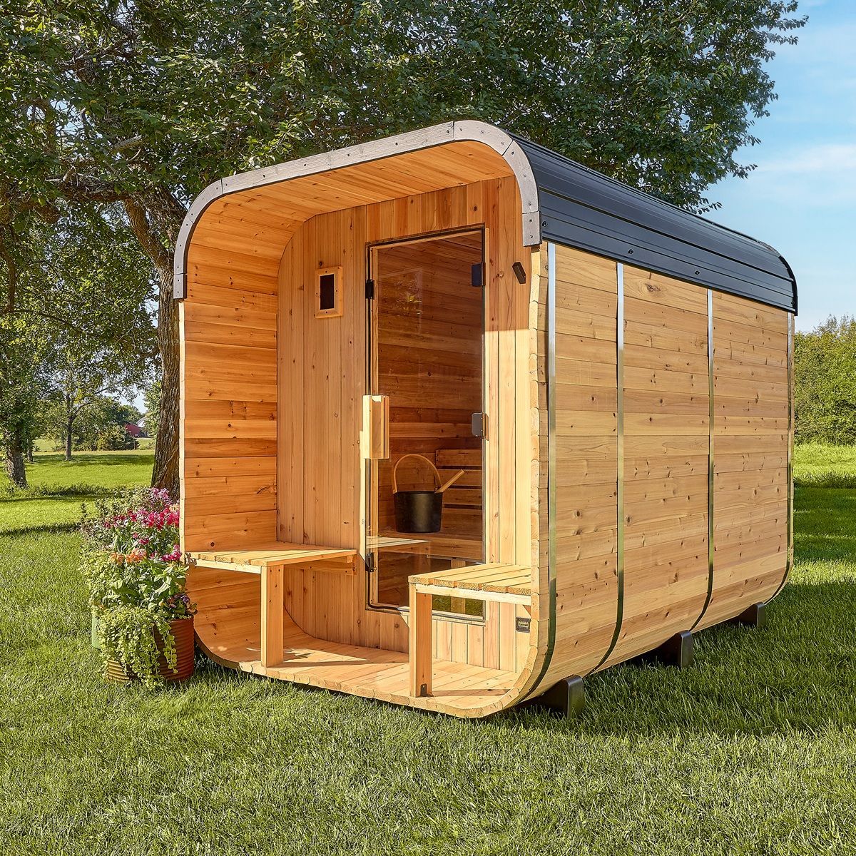 Small wooden tiny house on grass with open front door, rounded roof, and trees in the background