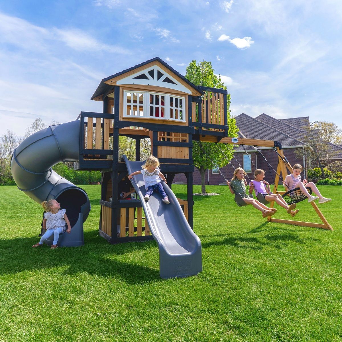 Children playing on a backyard playset with a slide and swings on a sunny lawn