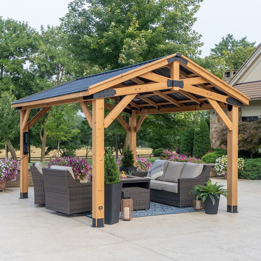 Wooden outdoor gazebo with solar roof panels and wicker seating on a patio, surrounded by greenery