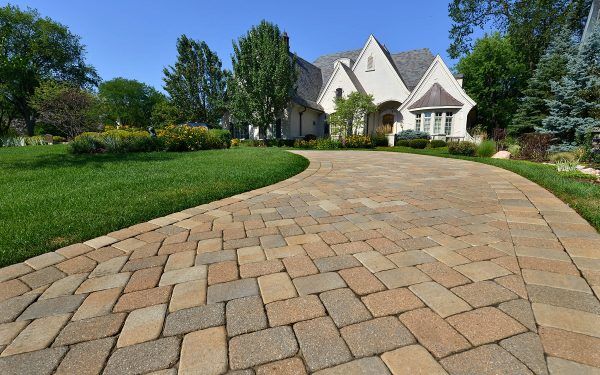Curved stone driveway leading to a large suburban house with manicured lawn and trees