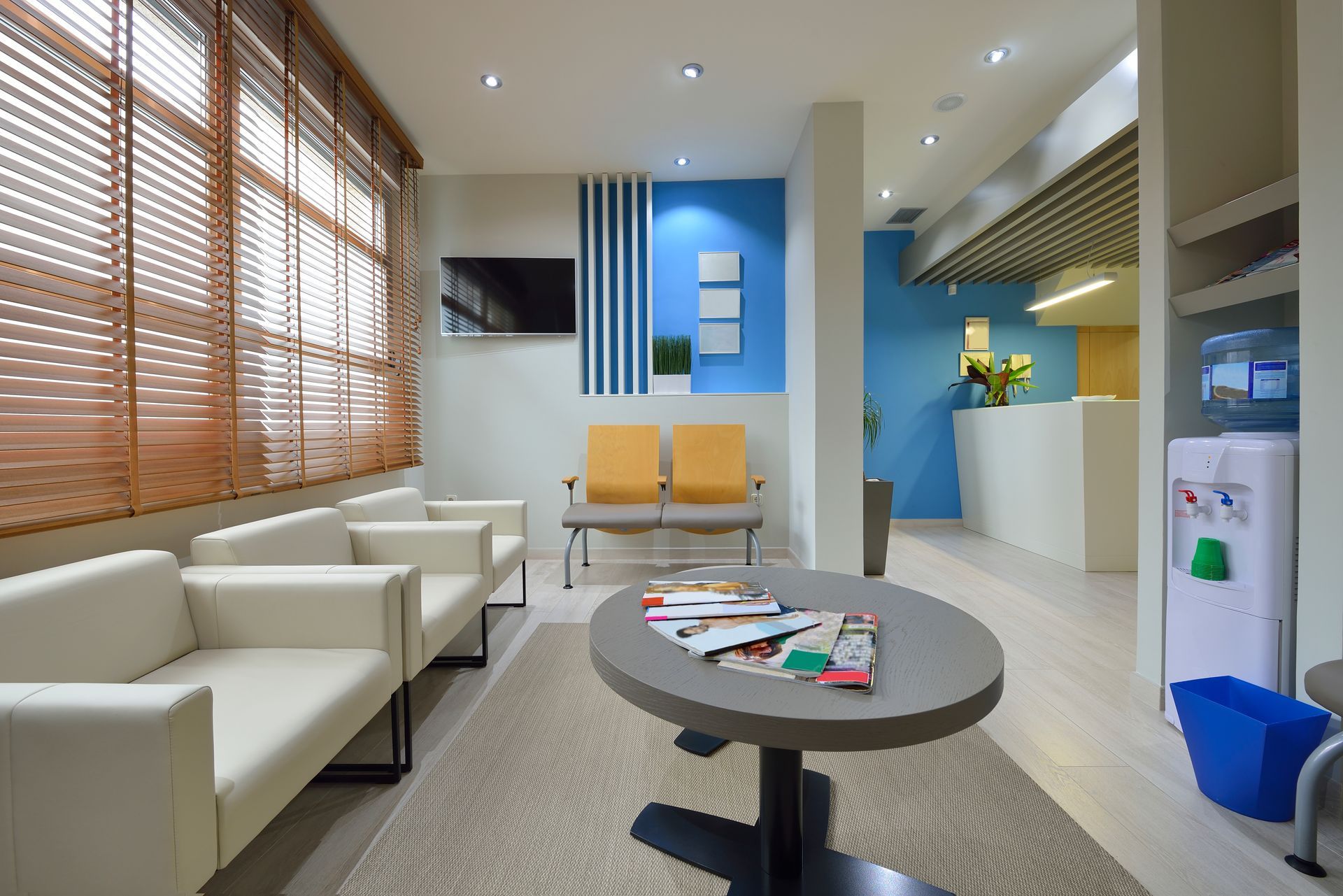 A contemporary waiting room with accent blue walls and wooden blinds for window treatments
