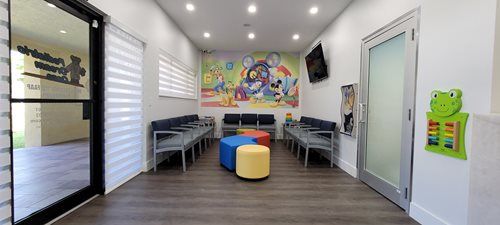 A children's dental office waiting room with colorful mural, chairs, and play area.