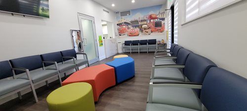 A brightly lit pediatric waiting room with colorful seating and Cars-themed wall mural.