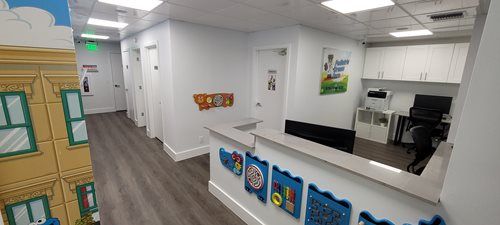 An office waiting area with a reception desk, doors, and Sesame Street-themed wall decor.