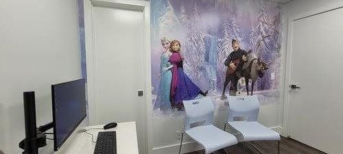 A room with a Frozen mural, white chairs, and a computer monitor.