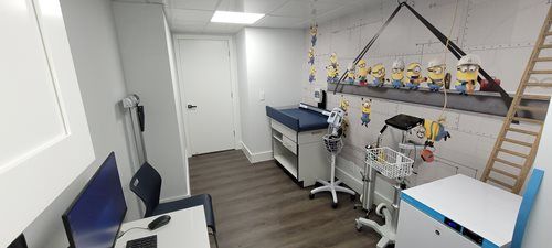 A child's doctor's office. Minion wallpaper, changing table, exam equipment, and a computer desk.