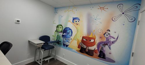 Room with Inside Out characters Joy, Sadness, Anger, Fear, Disgust on the wall. A small desk, stool, and chair are visible.