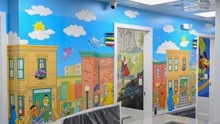 Sesame Street mural in hallway with blue sky, buildings, characters, and clouds.