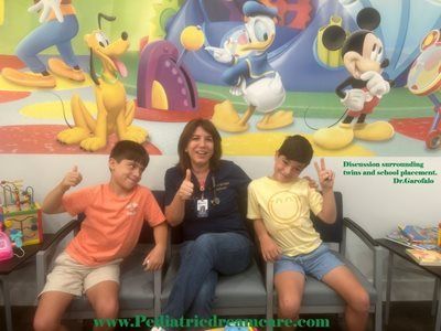 Two boys and a woman giving thumbs up in a pediatric waiting room with Disney characters on the wall.
