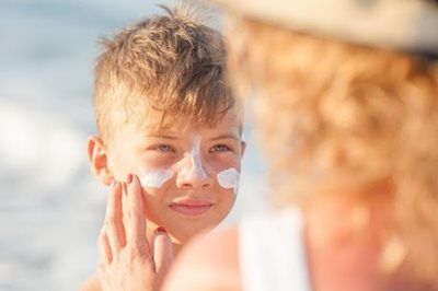 Person applying sunscreen to a child's face at the beach.