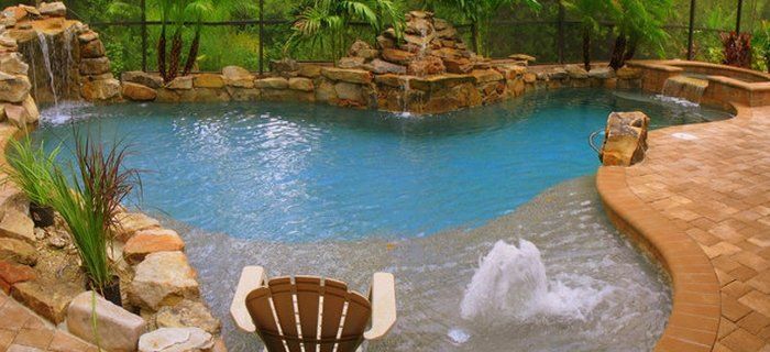 A large swimming pool with a waterfall in the background and a chair in the foreground.