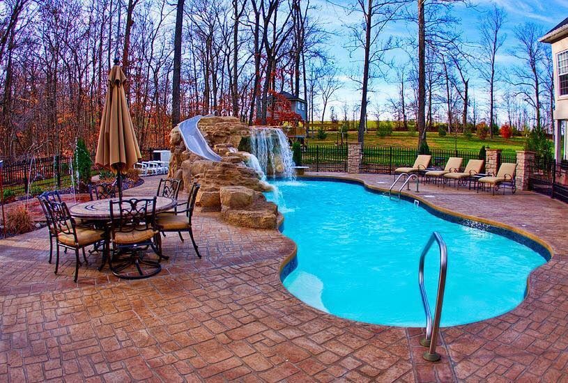 A large swimming pool with a water slide and a table and chairs around it.