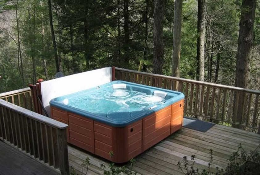 A hot tub is on a wooden deck in the woods