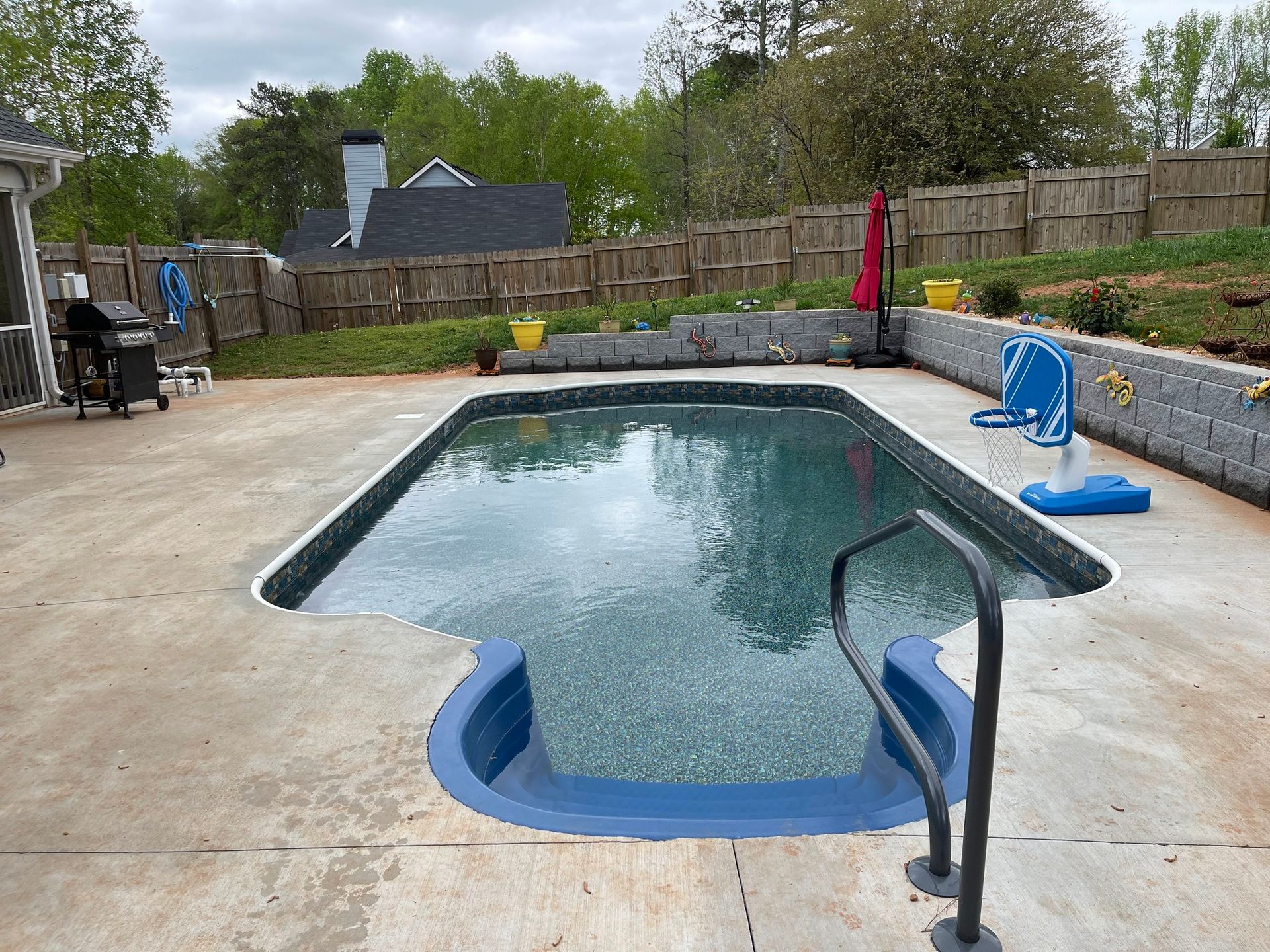 Backyard swimming pool with a blue cover, concrete deck, and fenced yard