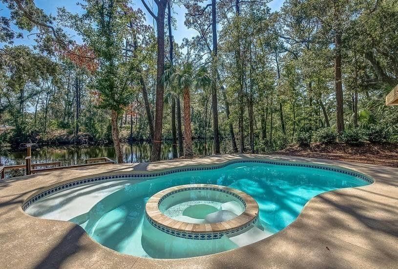 Backyard pool with a circular hot tub, surrounded by a wood deck and tall pine trees