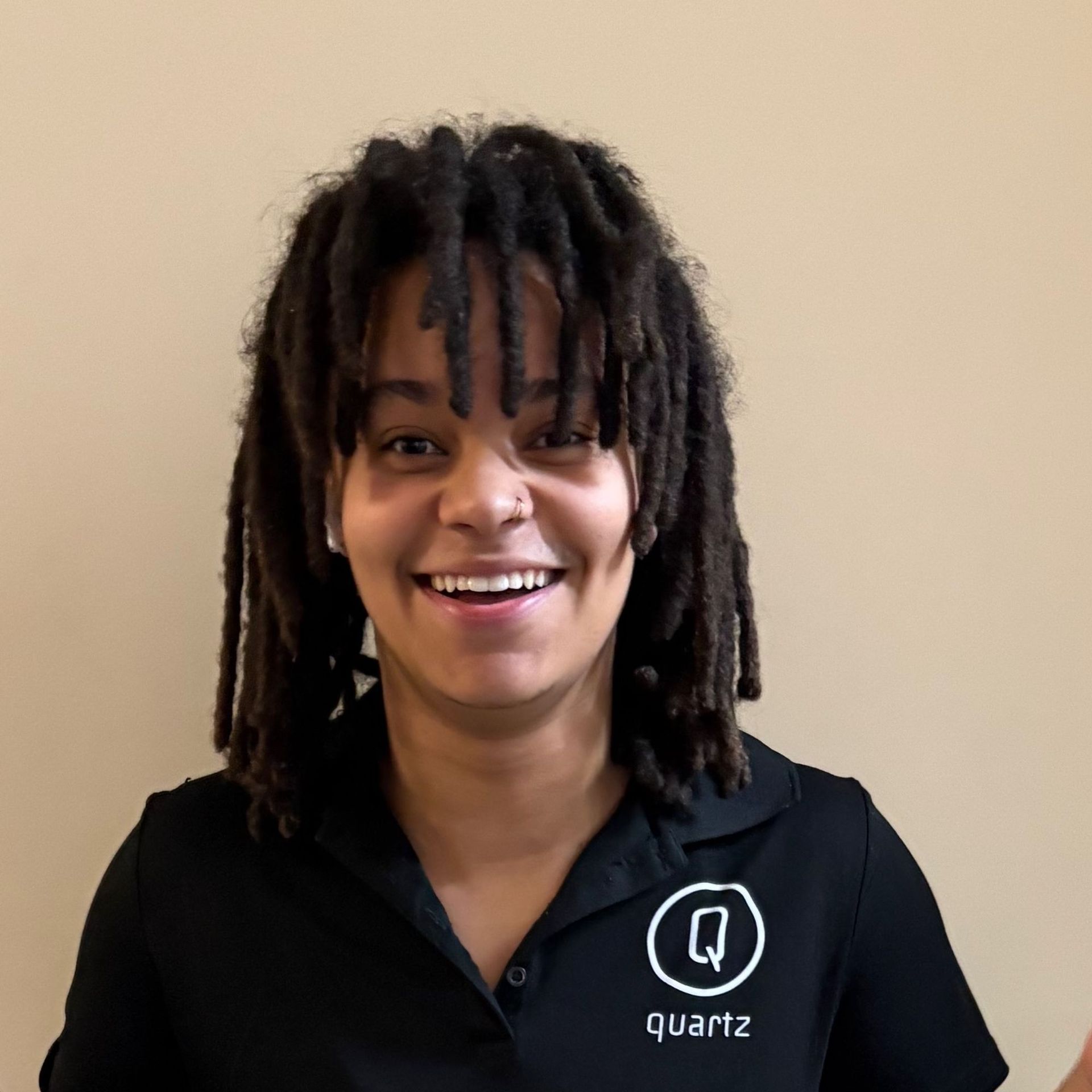 Smiling person in a black Quartz polo shirt against a plain beige wall