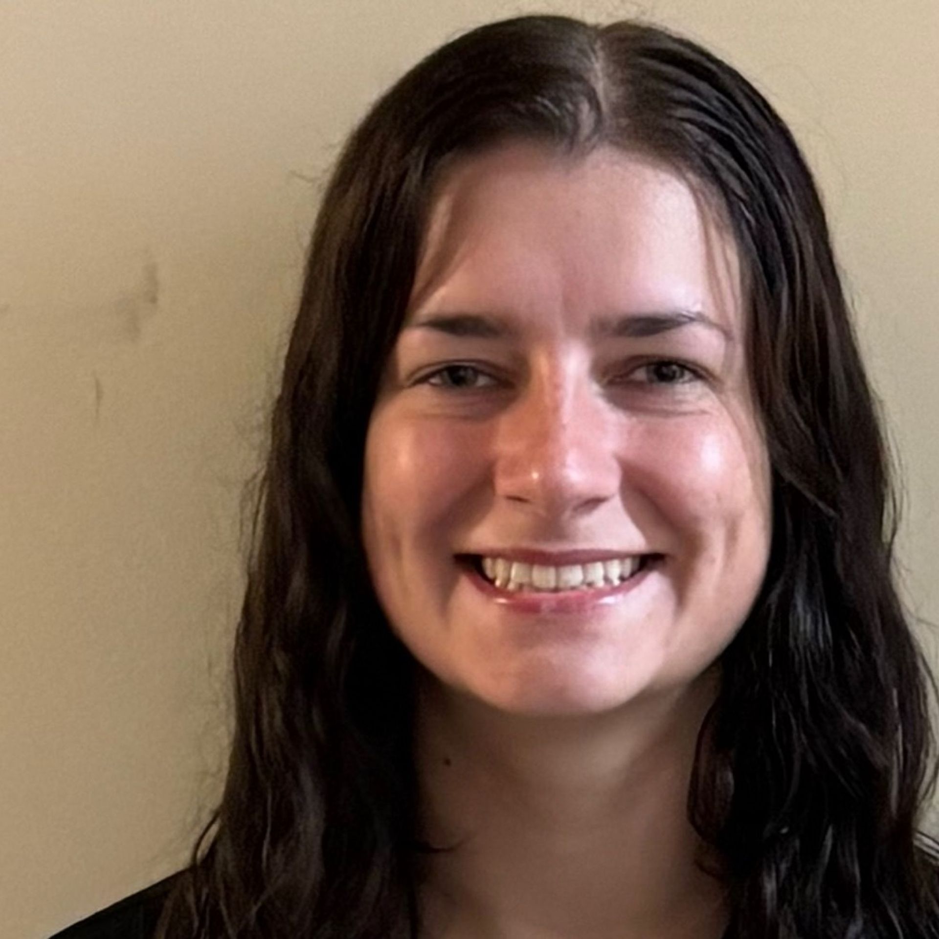 Smiling person with dark hair against a plain beige wall