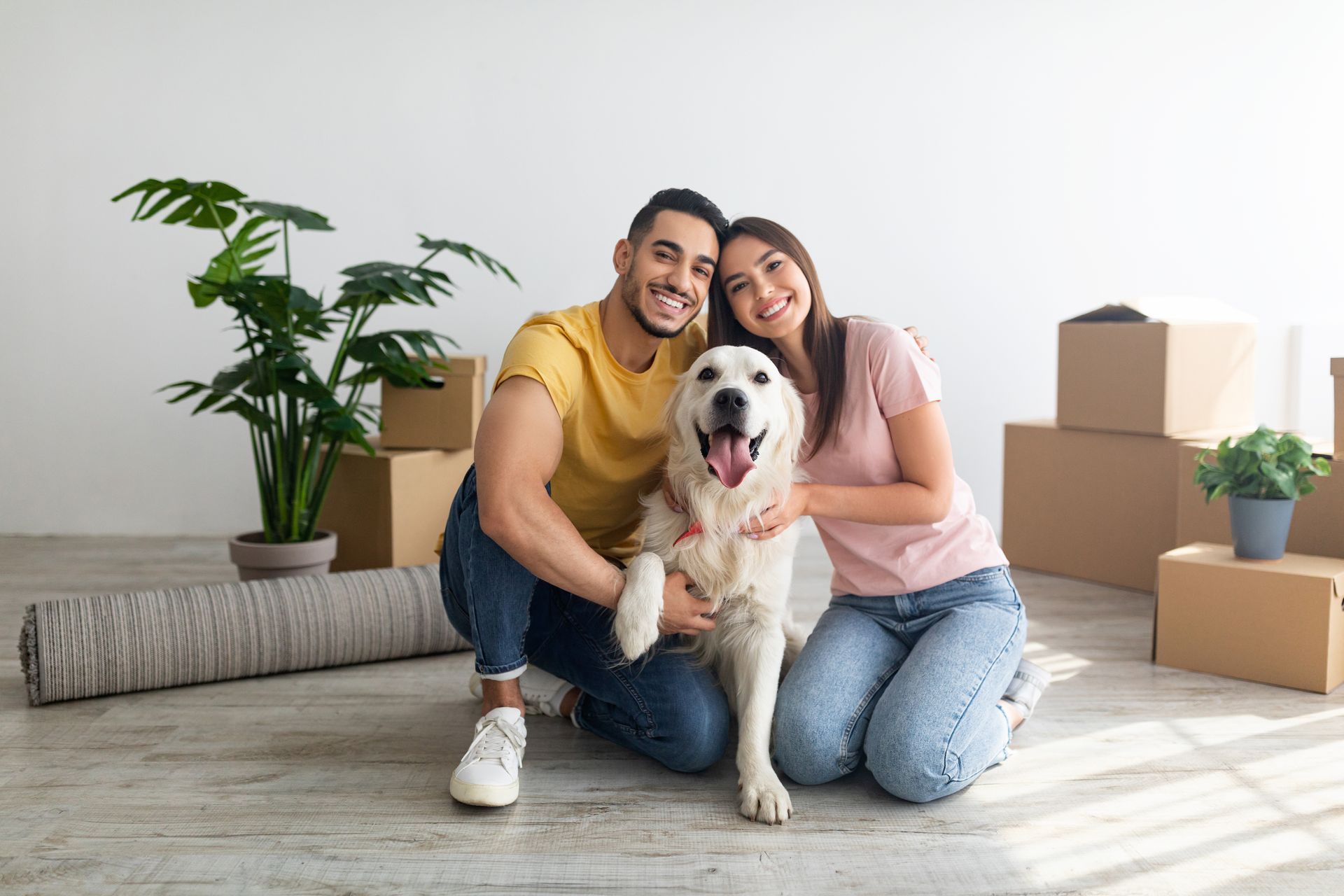 Two people cleaning a bright living room, one sweeping near a cardboard box and couch