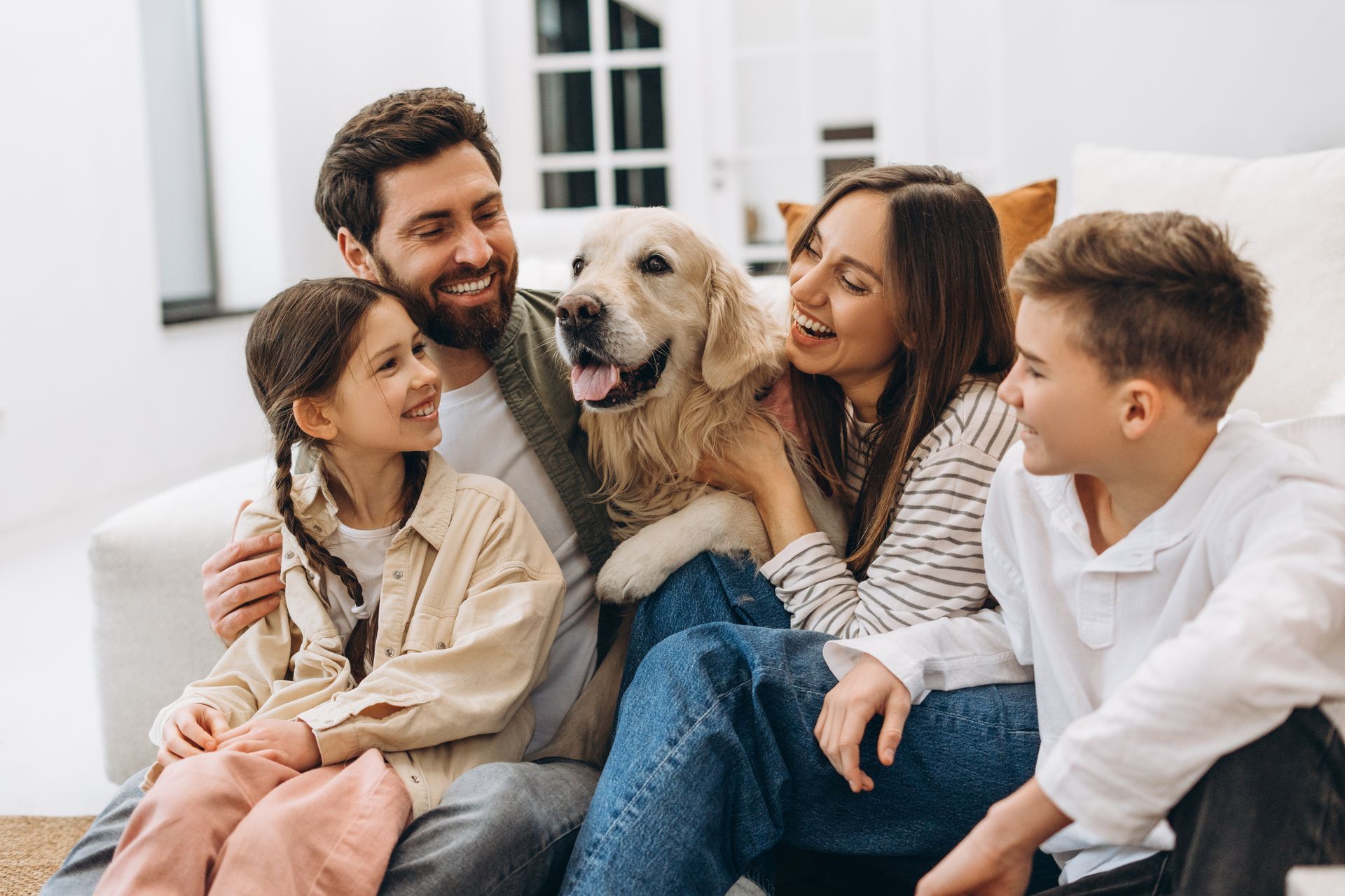 Family sitting on a couch with a happy dog in a bright living room