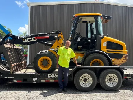 Man standing beside a yellow JCB loader on a flatbed trailer outdoors