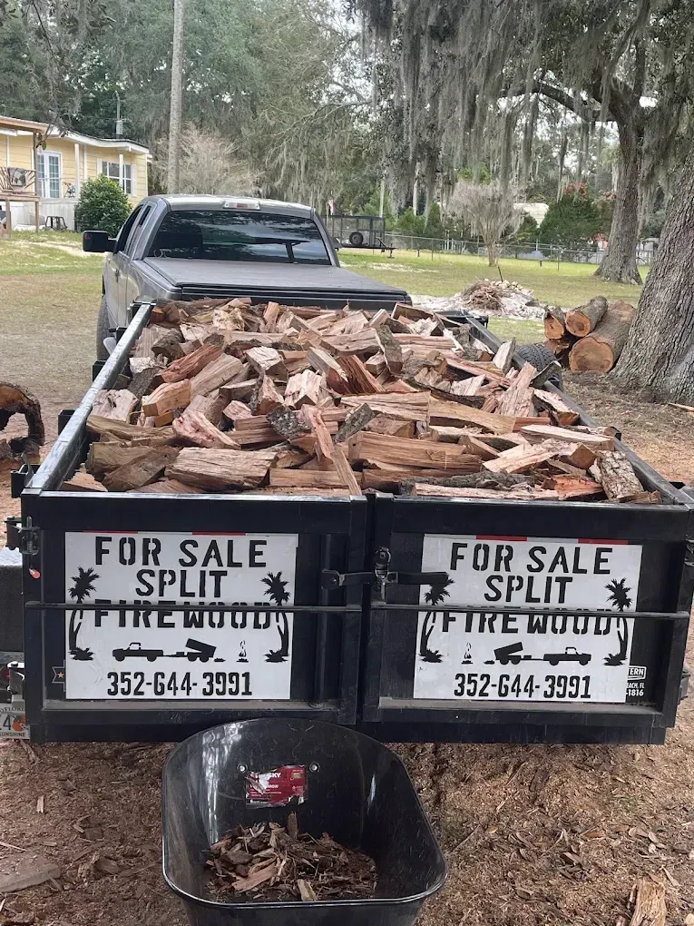 Pickup truck loaded with split firewood for sale in a driveway, with “FOR SALE SPLIT” signs on the tailgate.