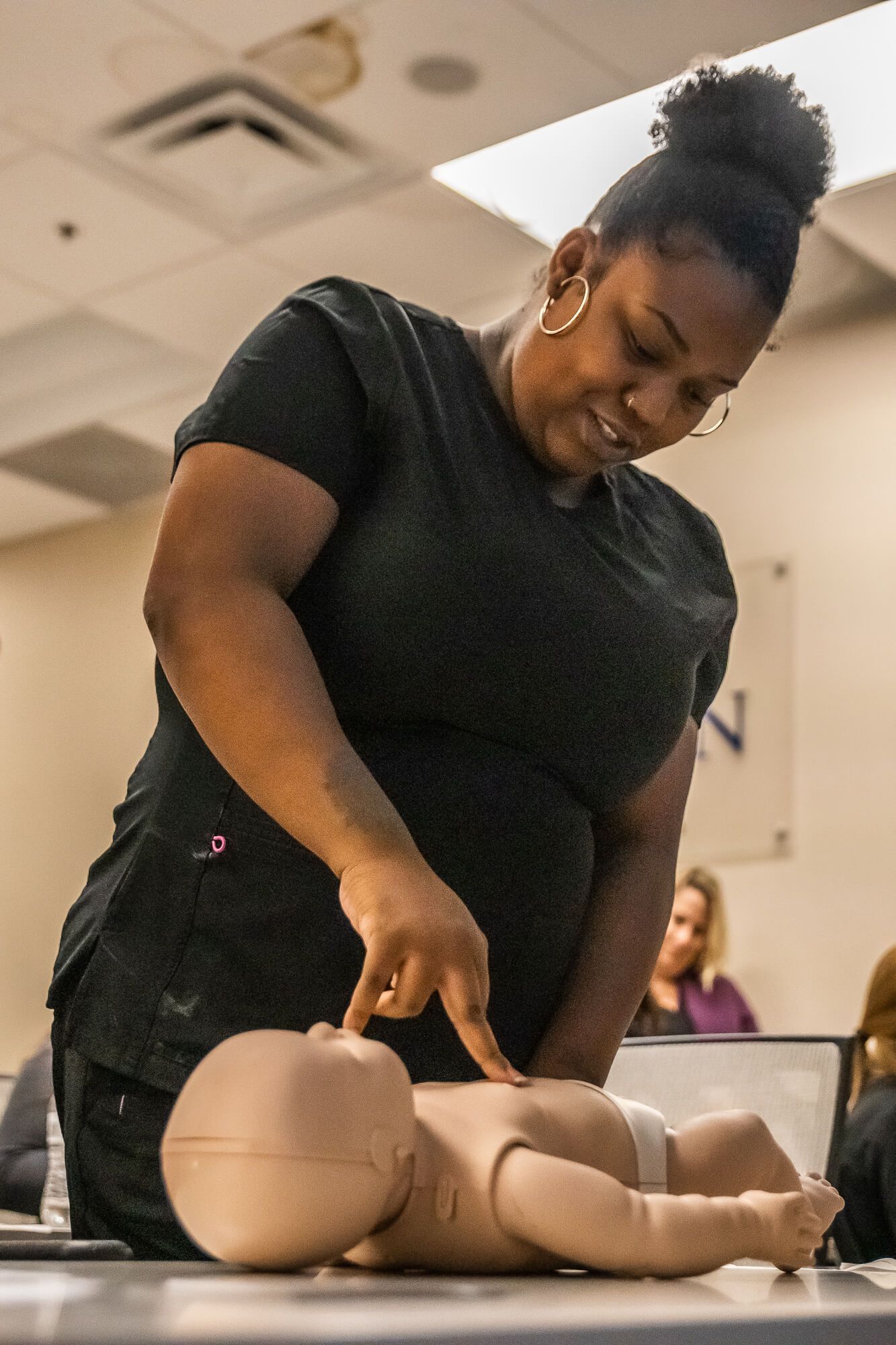 Groups & Corporate CPR Training: A woman is pointing at a baby doll on a table.