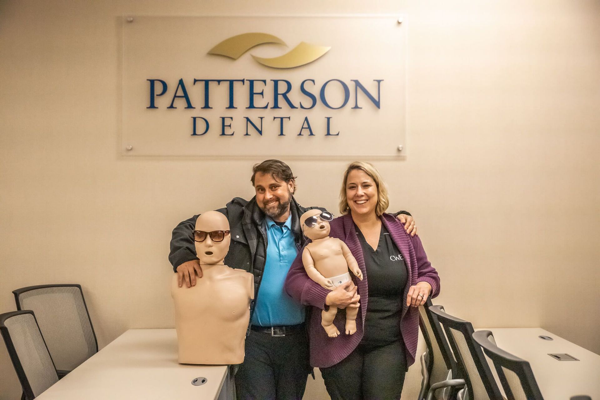 Groups & Corporate CPR Training: A man and woman are holding a baby in front of a patterson dental sign.