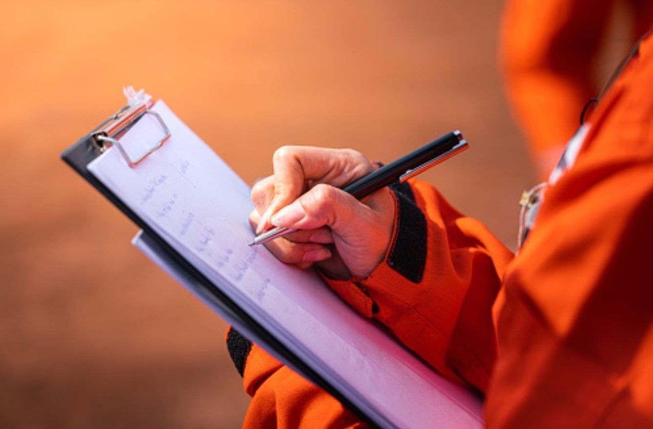A person is writing on a clipboard with a pen.