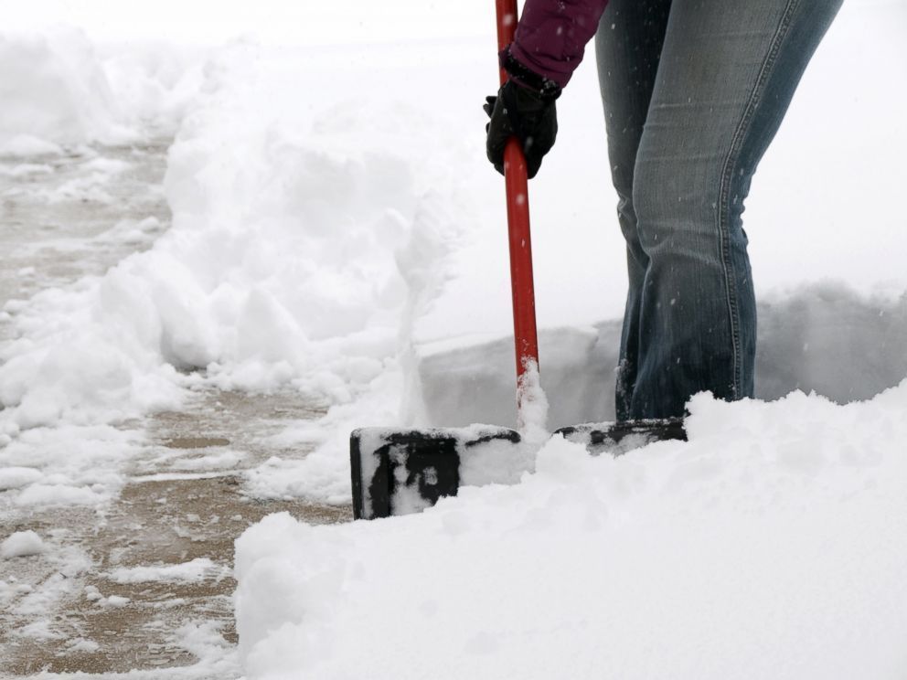 A person is shoveling snow on a sidewalk with a red handle