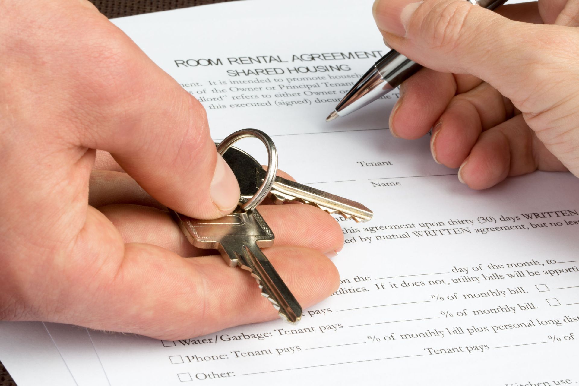 A person is holding keys and signing a lease agreement