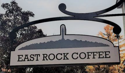 A sign for east rock coffee hangs from a building