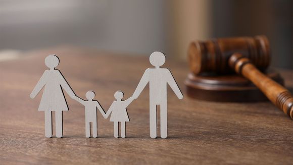 Paper family cutouts on a wooden table beside a judge’s gavel, symbolizing family law.