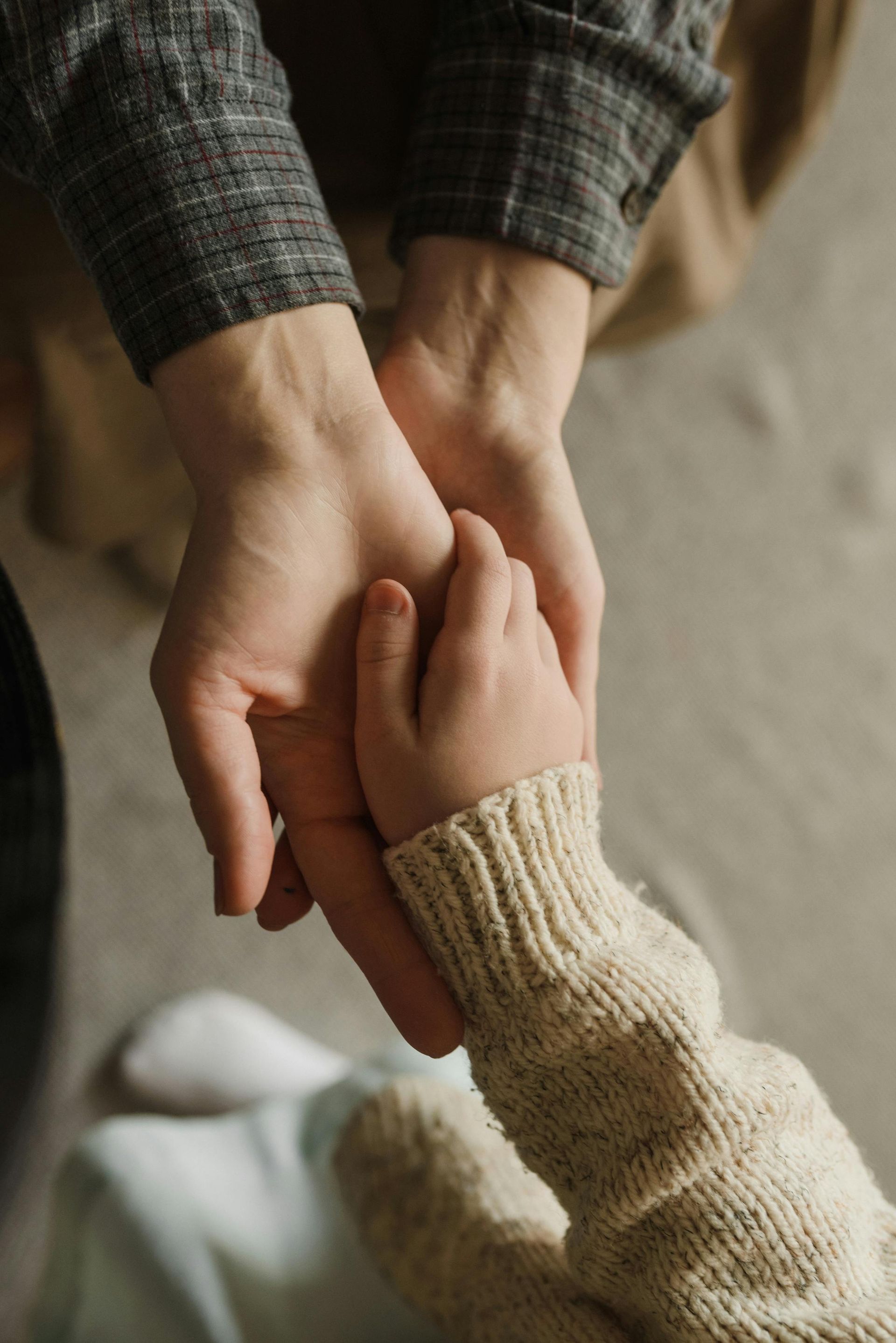 Two hands gently holding a child’s hand, close-up in warm light