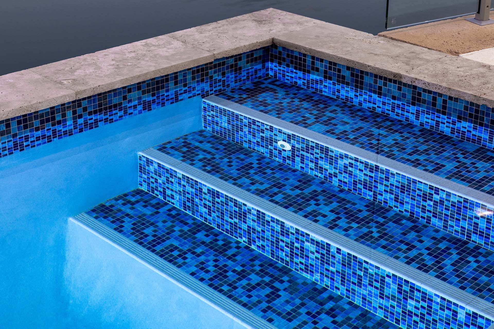 A swimming pool with blue tiles and stairs leading up to it.