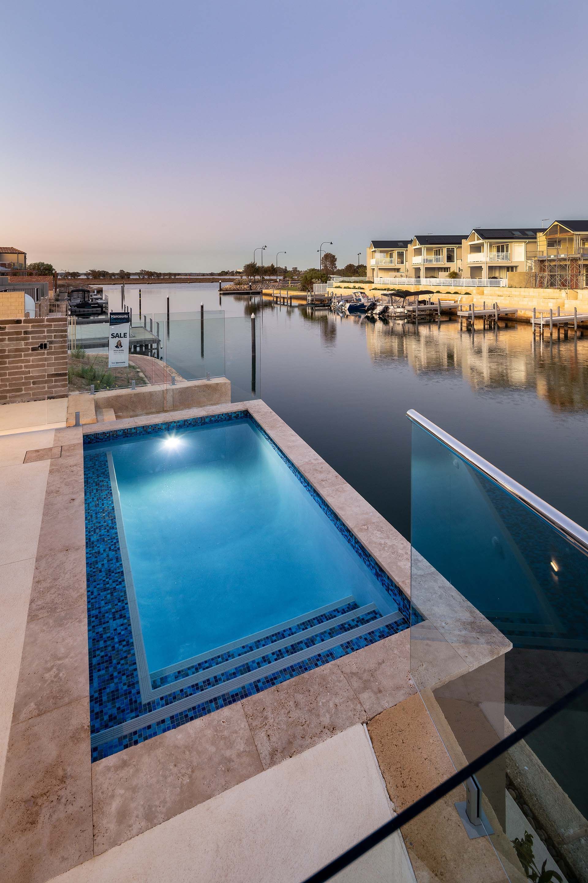 A large swimming pool is surrounded by a glass railing overlooking a body of water.