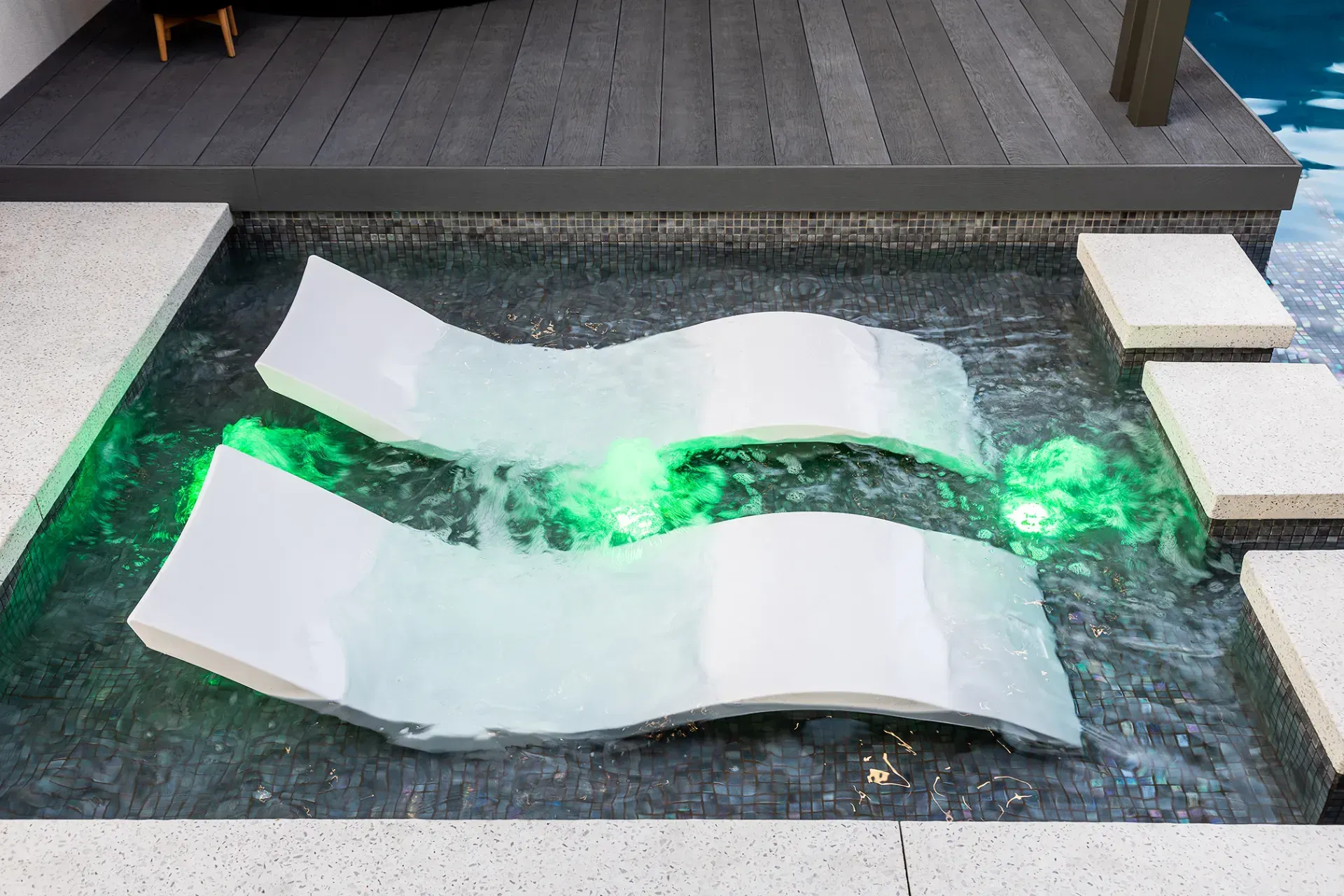 Two lounge chairs are floating in a pool with green lights.