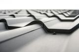 Close-up of a dark gray metal roof with a repeating wave-like pattern, against a white sky.