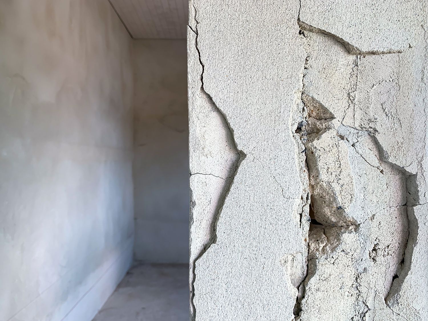 A corner of a room with a cracked wall and a hole in the wall.