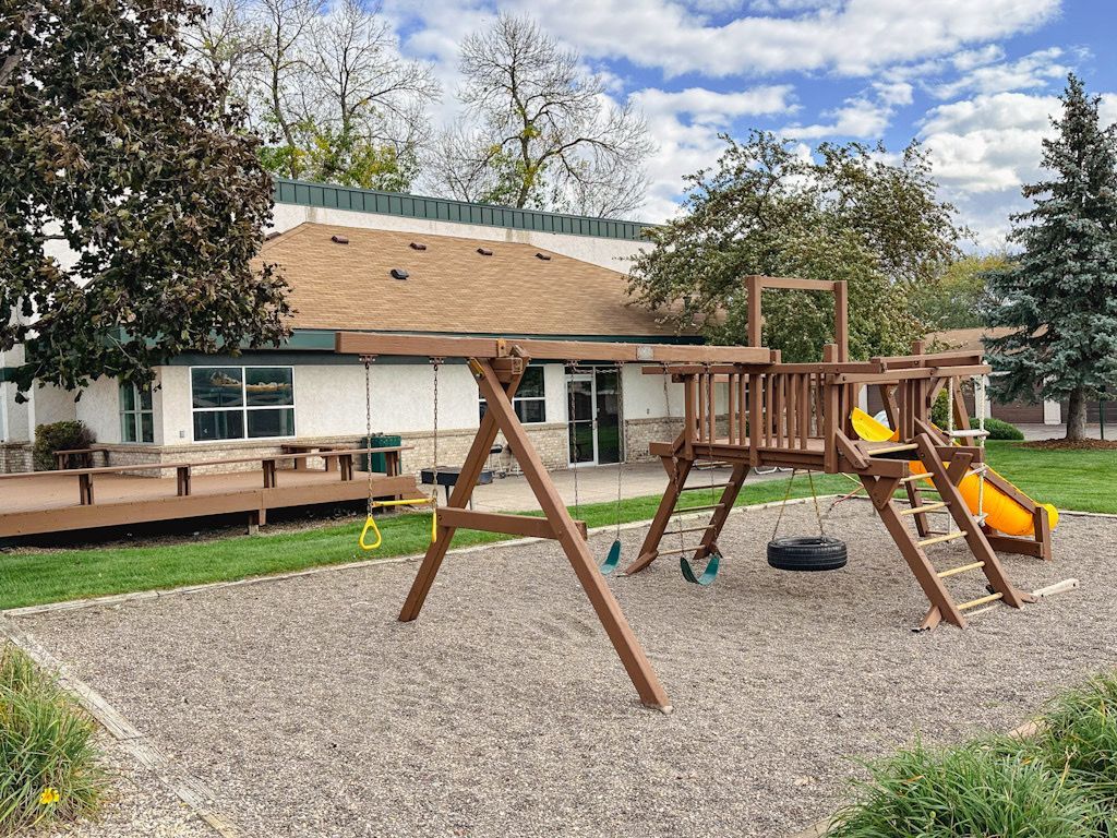 A wooden playground with a slide and swings in front of a house.