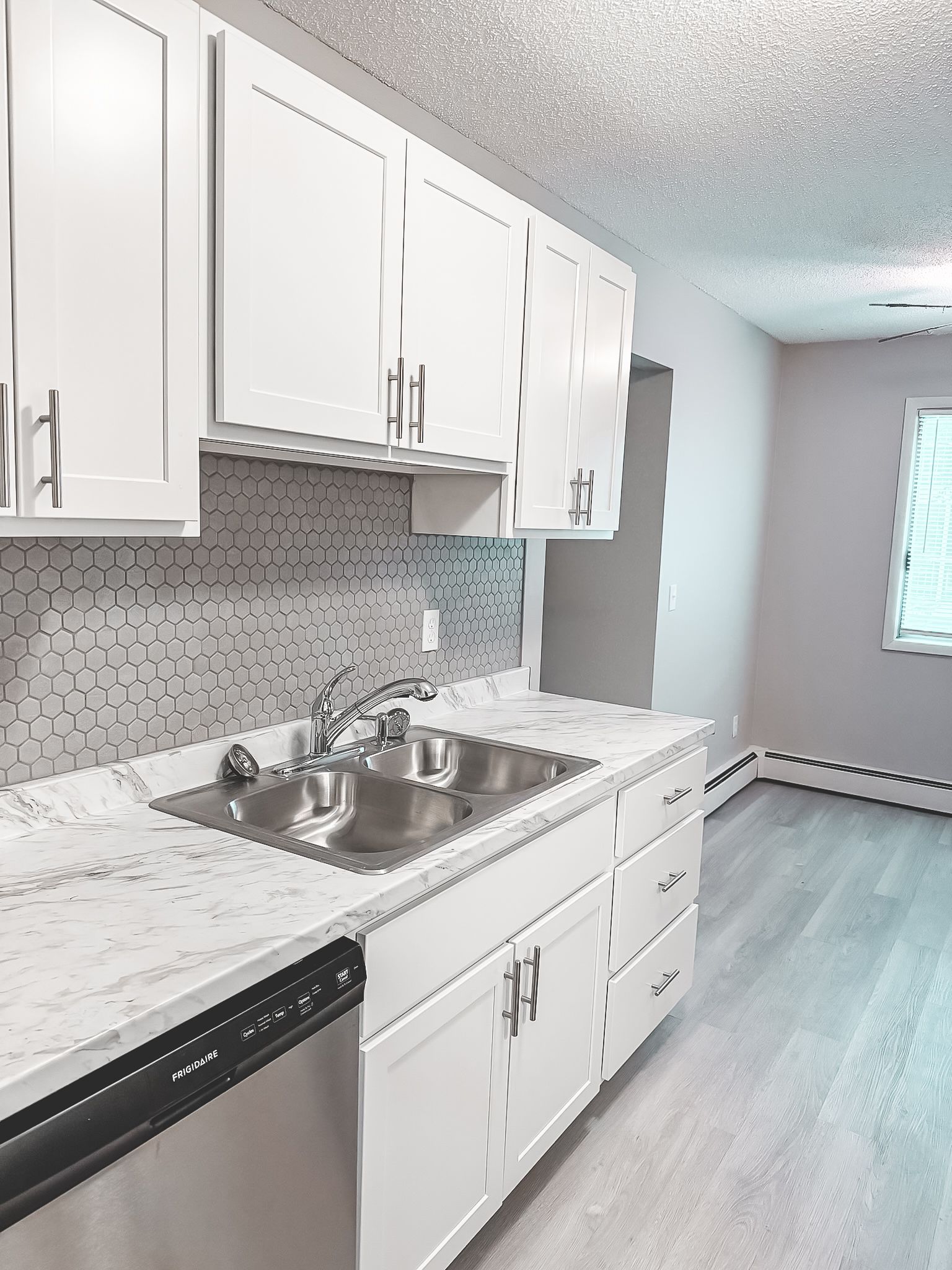 A kitchen with white cabinets , a sink , and a dishwasher.