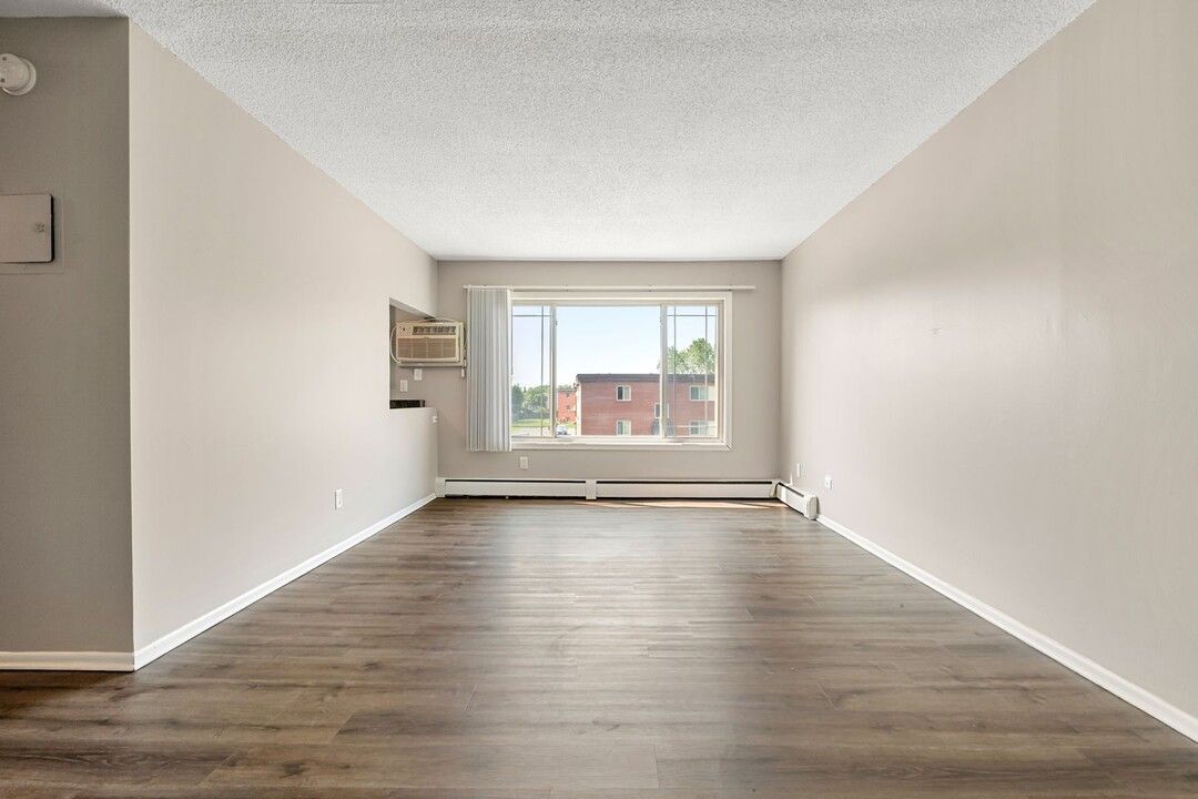 An empty living room with hardwood floors and a large window.