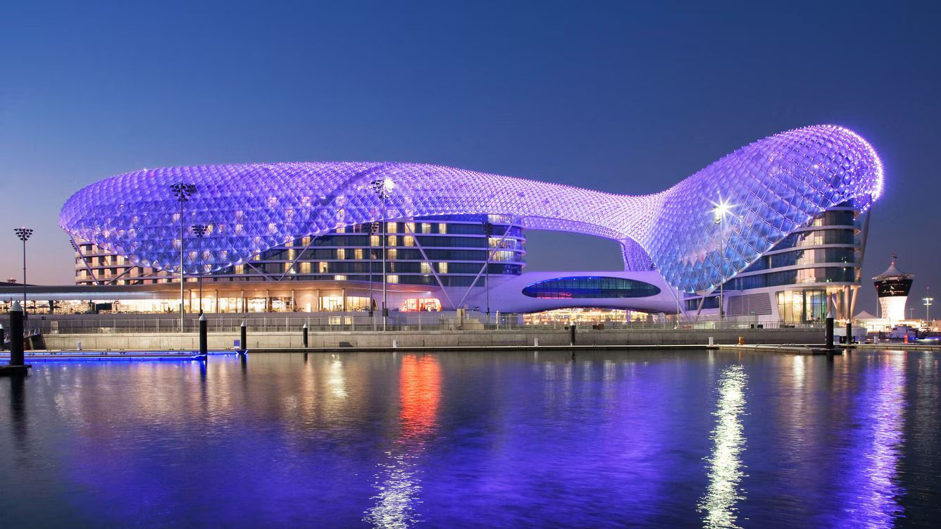 A large building is lit up in purple lights next to a body of water.