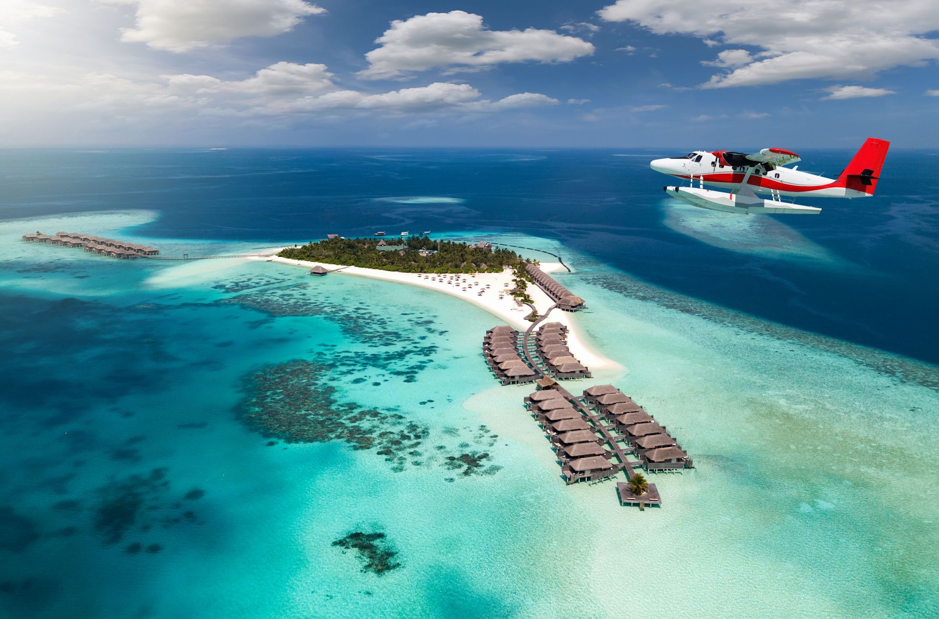 A Trans Maldivian Airways seaplane flying over a tiny island in the Maldives, surrounded by the Indian Ocean.