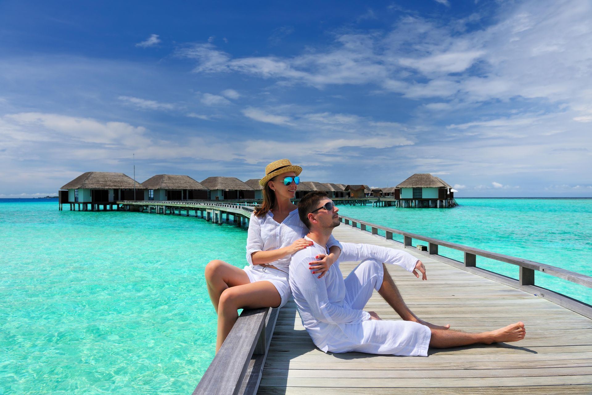 Couple in white on a beach jetty at Maldives in the Indian Ocean.