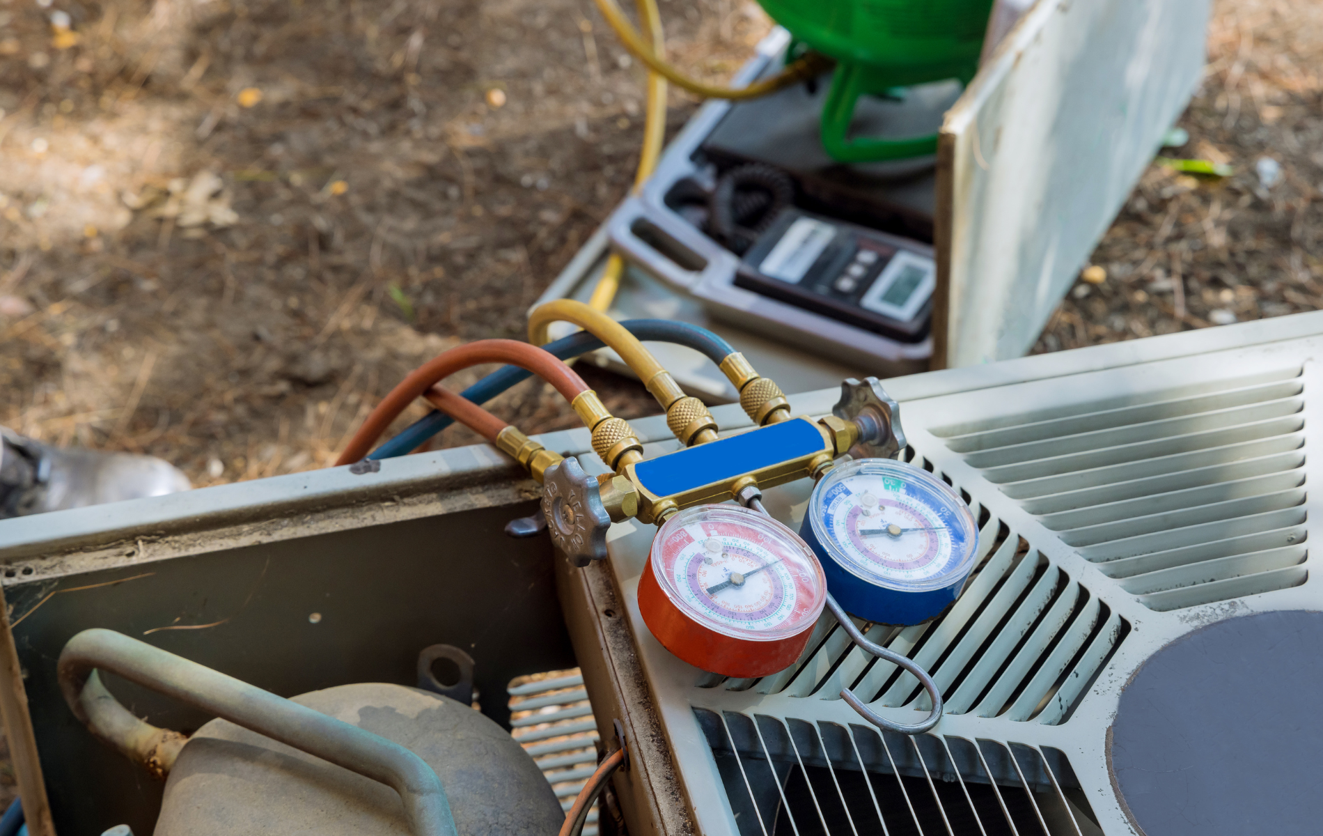 AC unit with gauges attached, likely being serviced outdoors. Red, blue, yellow hoses visible.
