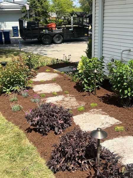Stone path through a landscaped garden with dark mulch, shrubs, and a trailer in the background.