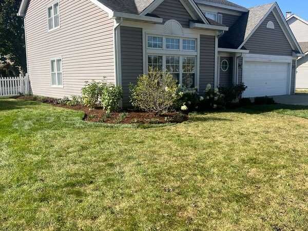 House with a green lawn and mulch beds. The house has gray siding and a white garage door.
