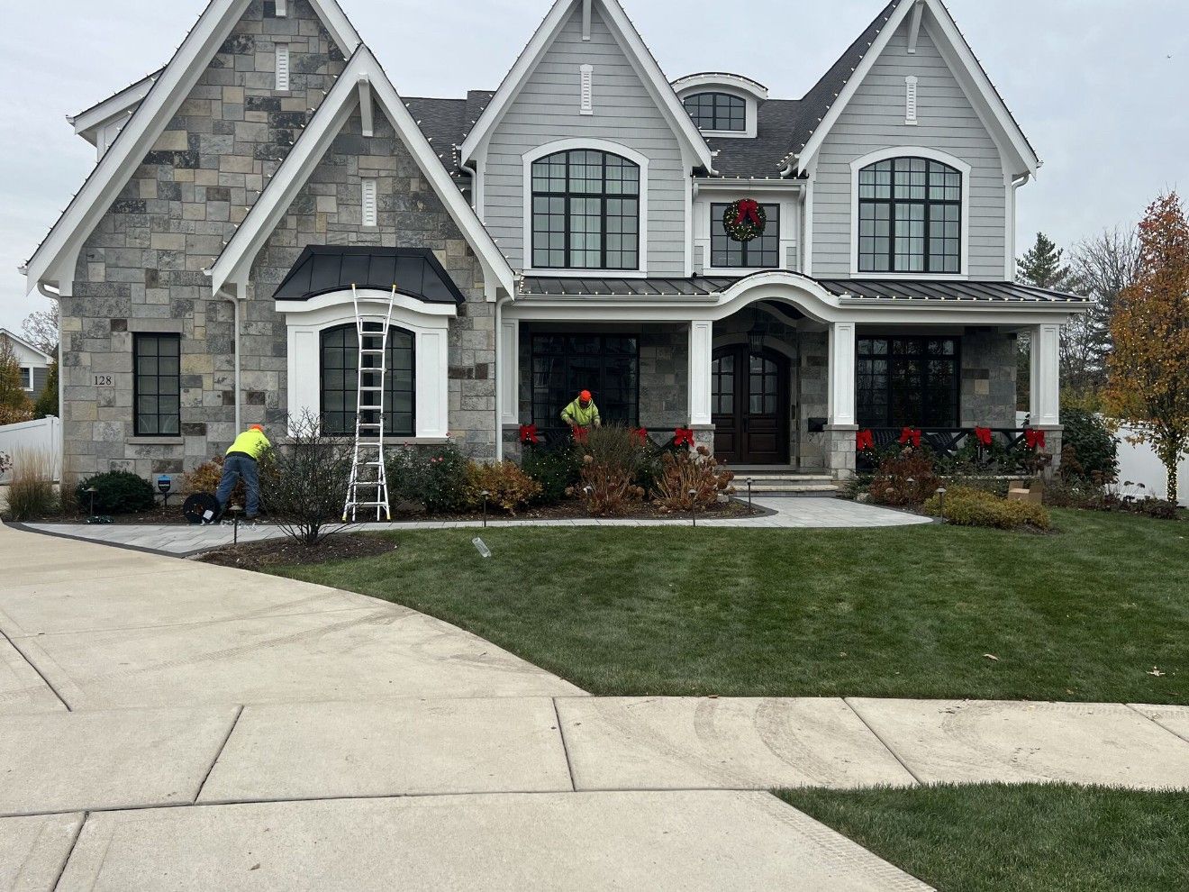 Stone and gray house with holiday decorations and two workers outside.