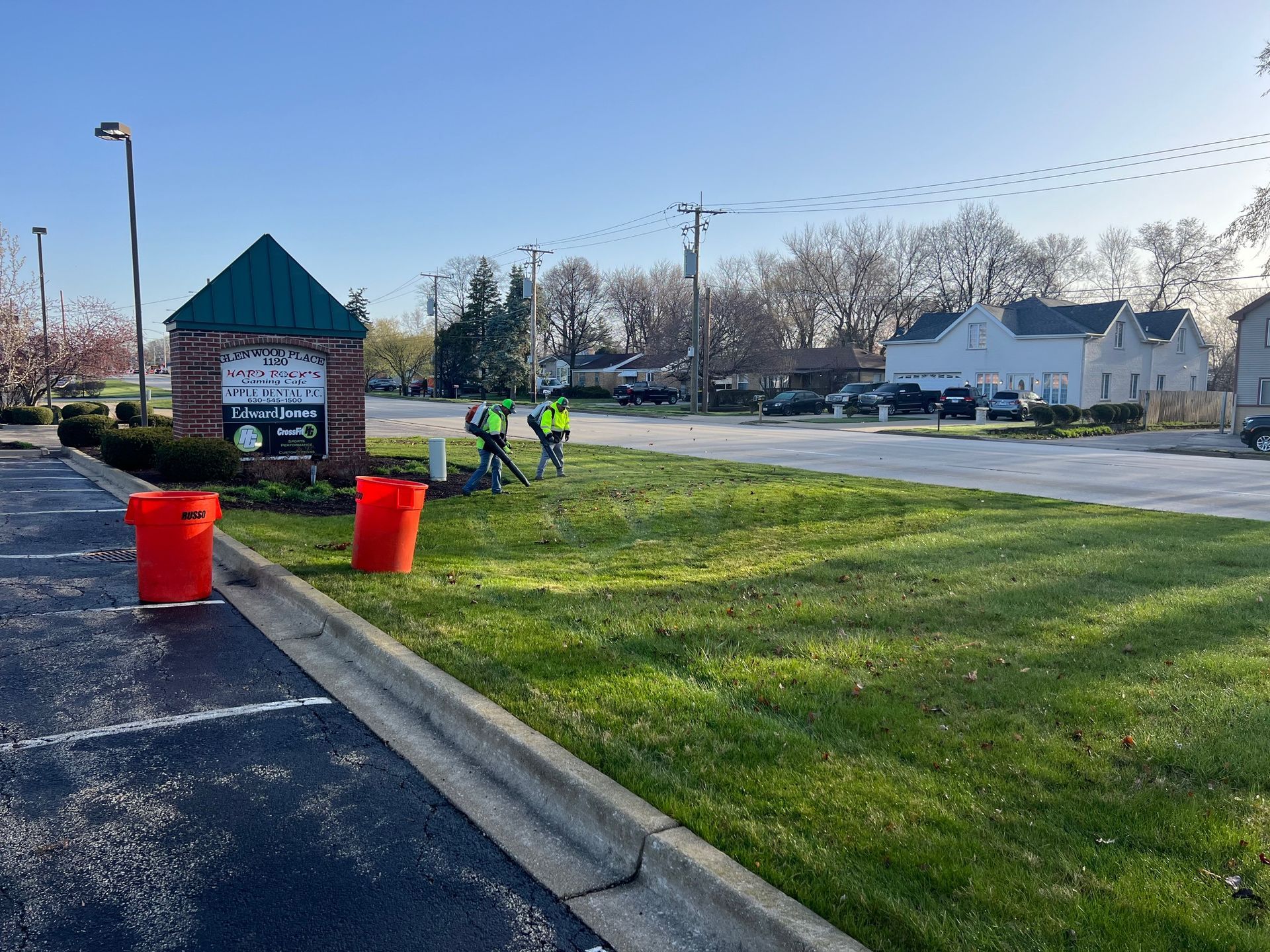 People in reflective vests weeding in front of a sign and green lawn. Red buckets sit nearby.