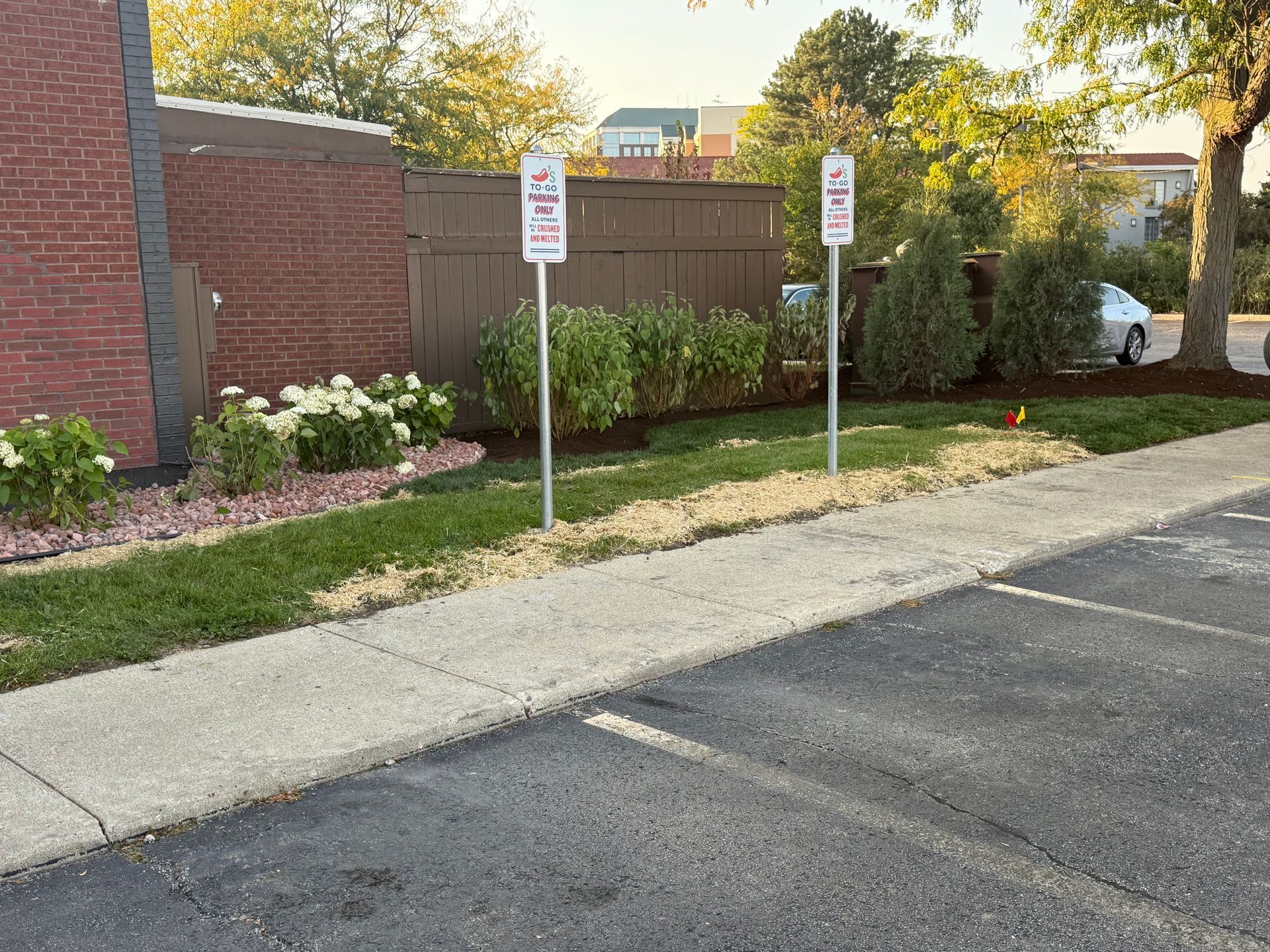 Two parking signs next to a landscaped area and a parking lot.